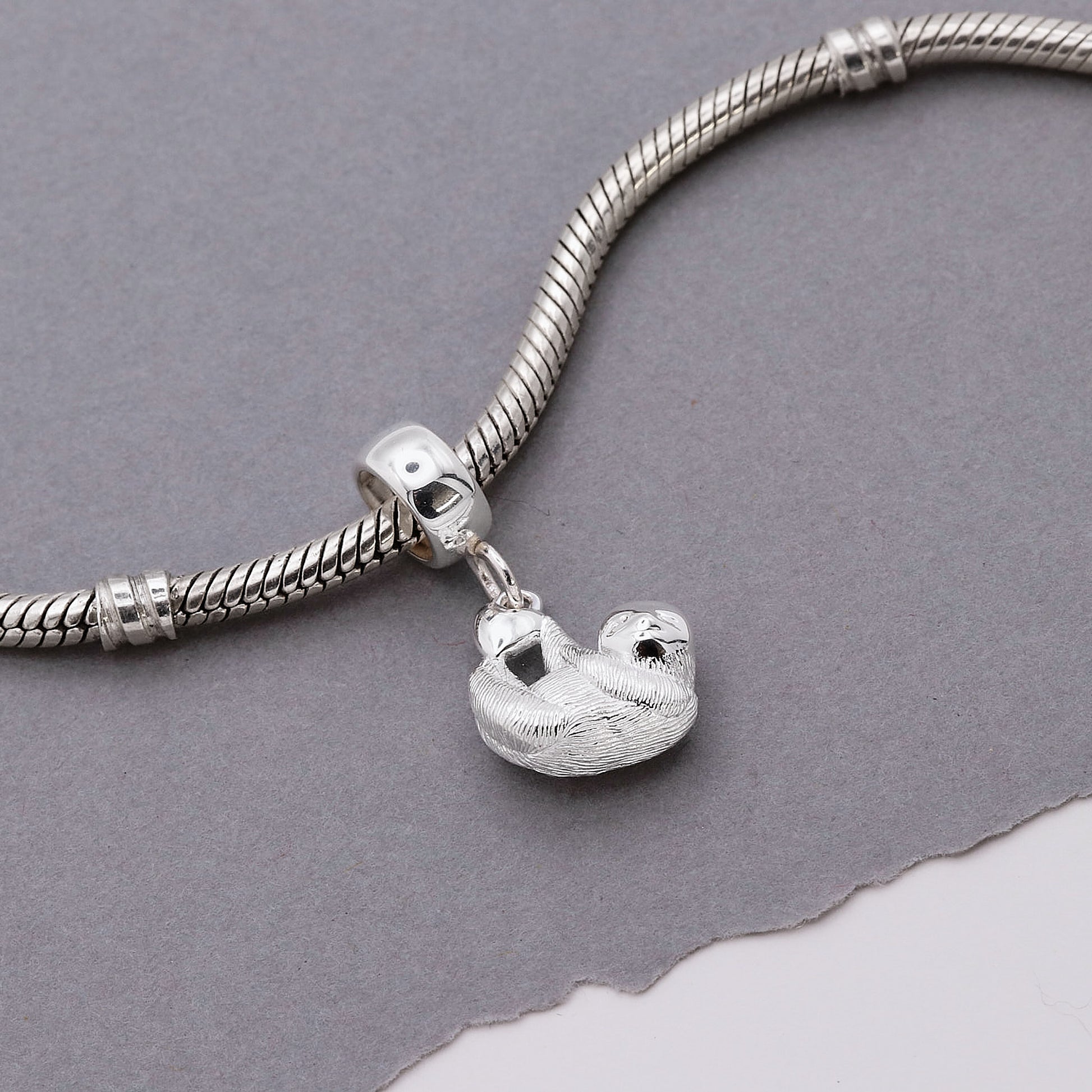 Silver bracelet with a sloth charm on a gray background