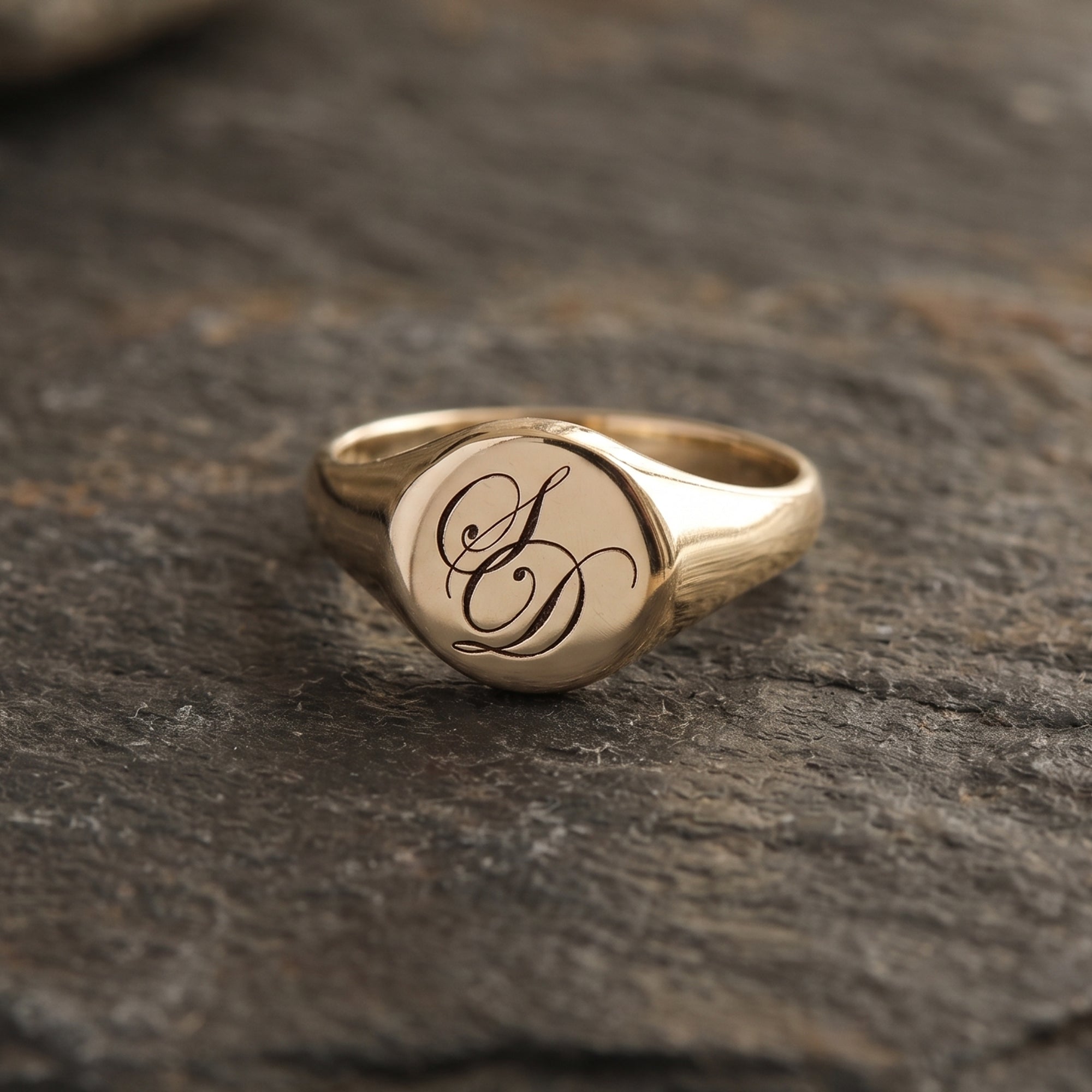 Gold ring with monogram on a dark stone surface