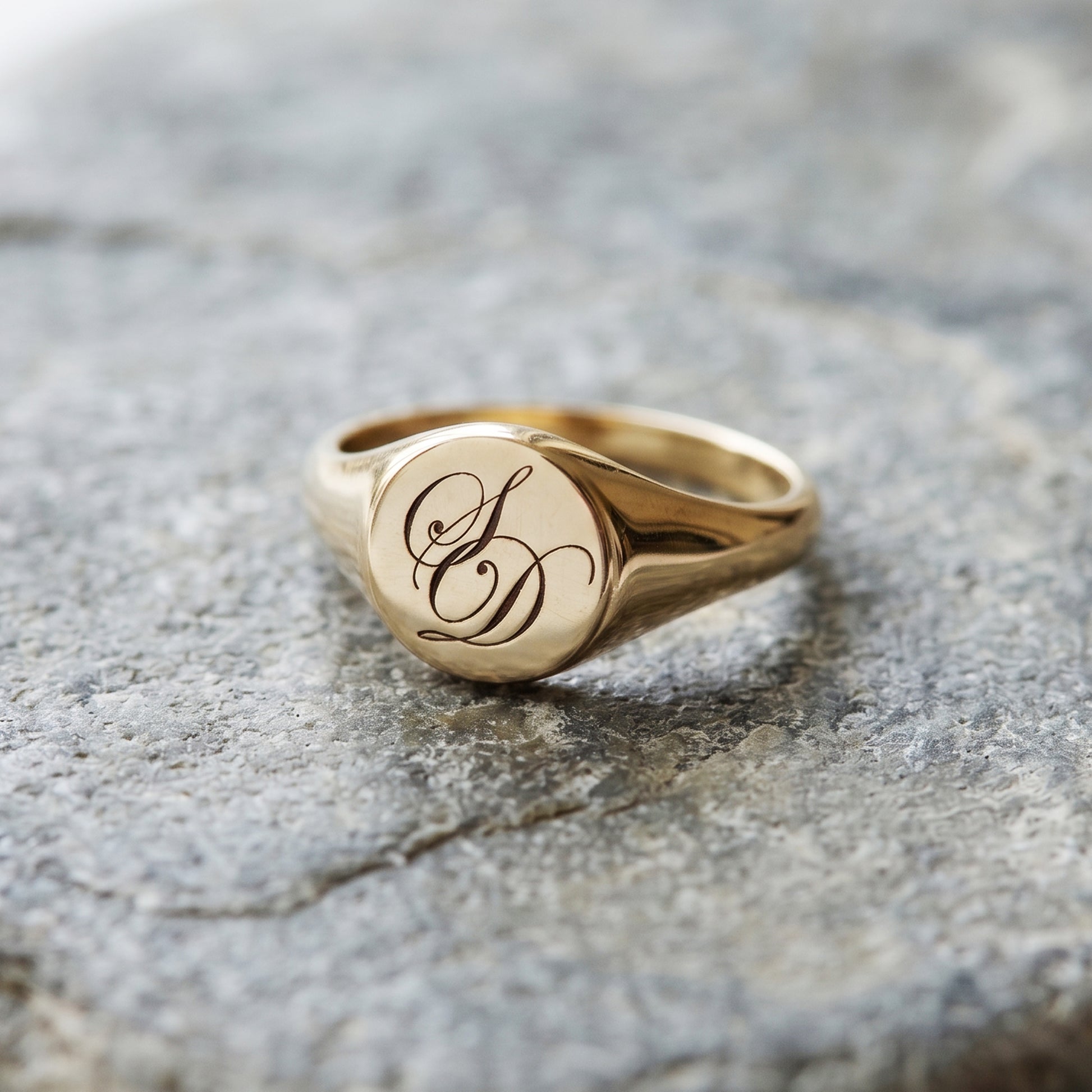 Gold ring with engraved initials on a textured stone surface
