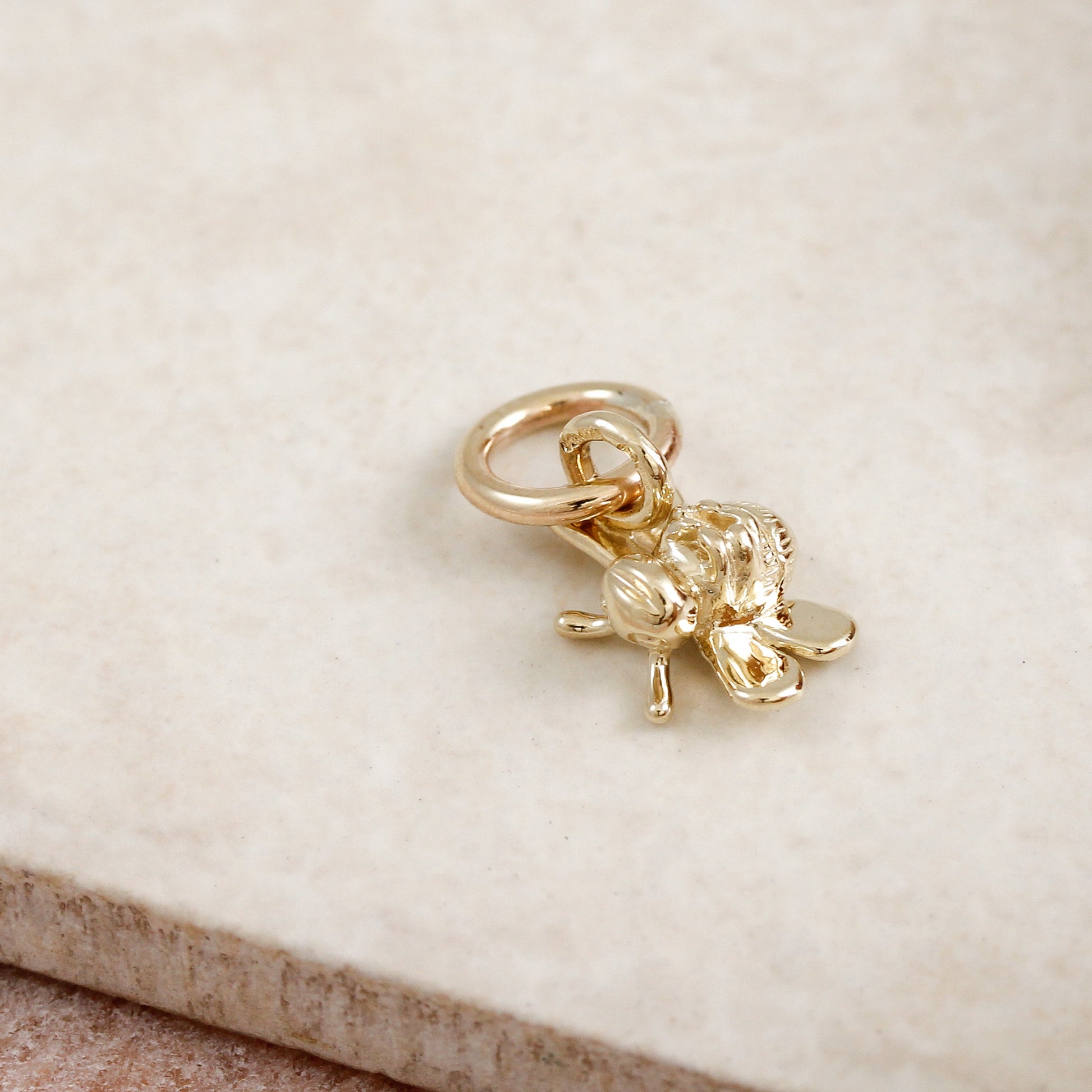 Gold bee charm on a beige stone surface