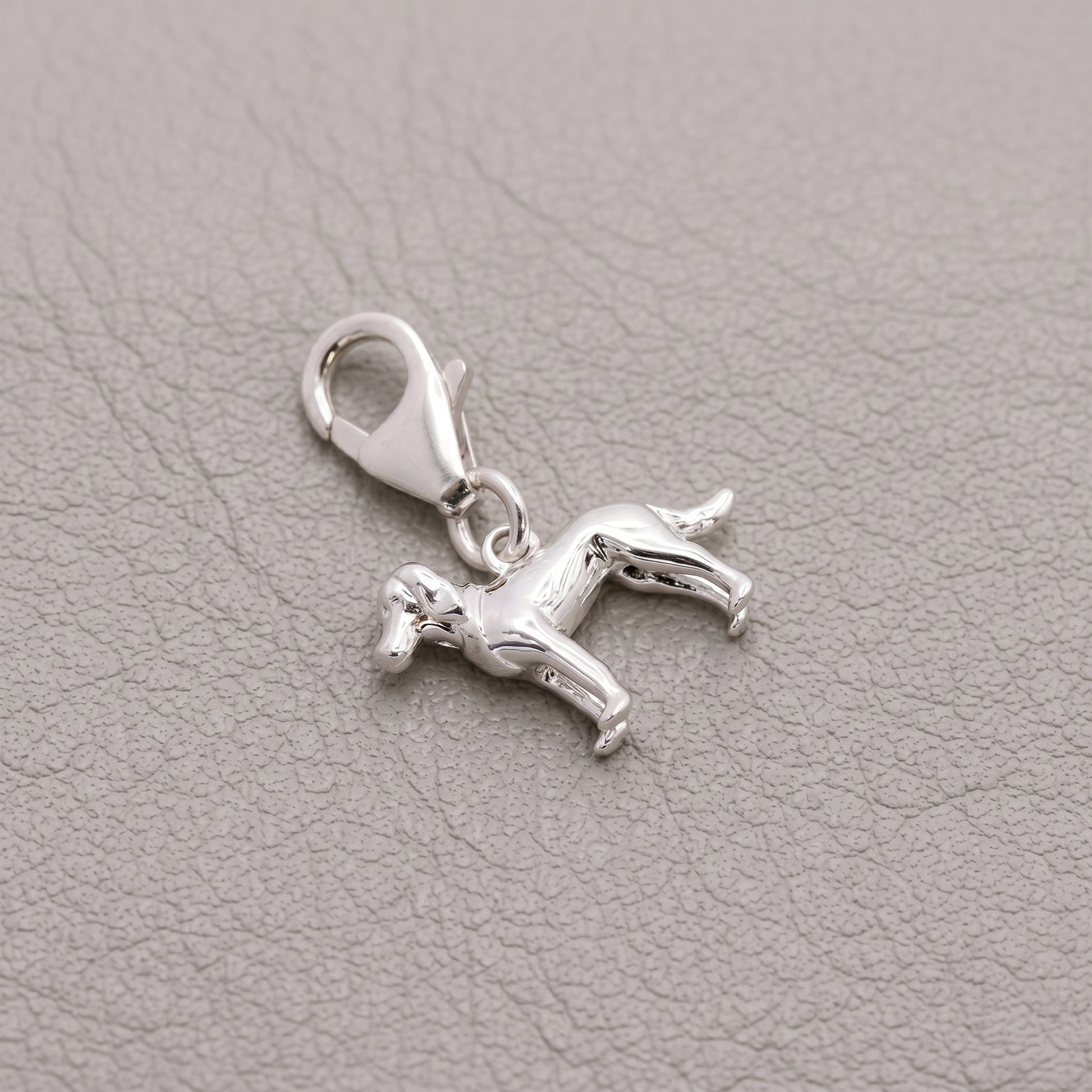 Silver horse charm with a clasp on a gray leather background