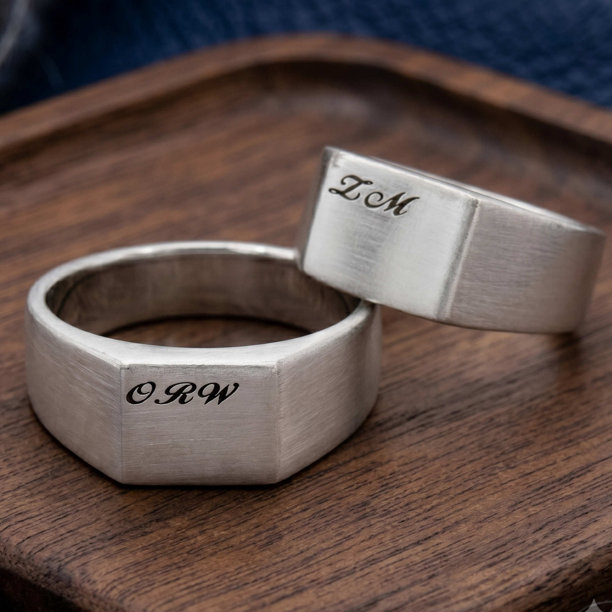 Two silver rings with engraved initials on a wooden surface