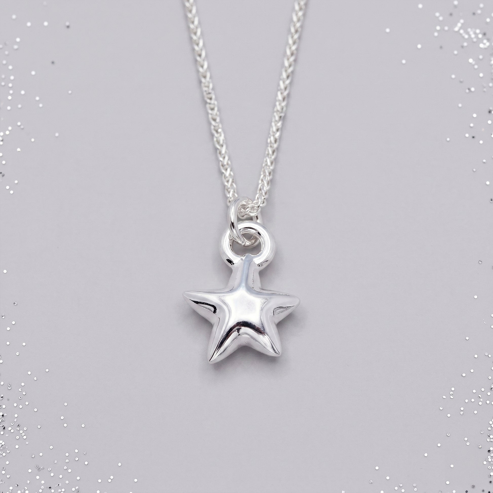 Silver star-shaped pendant on a chain against a gray background