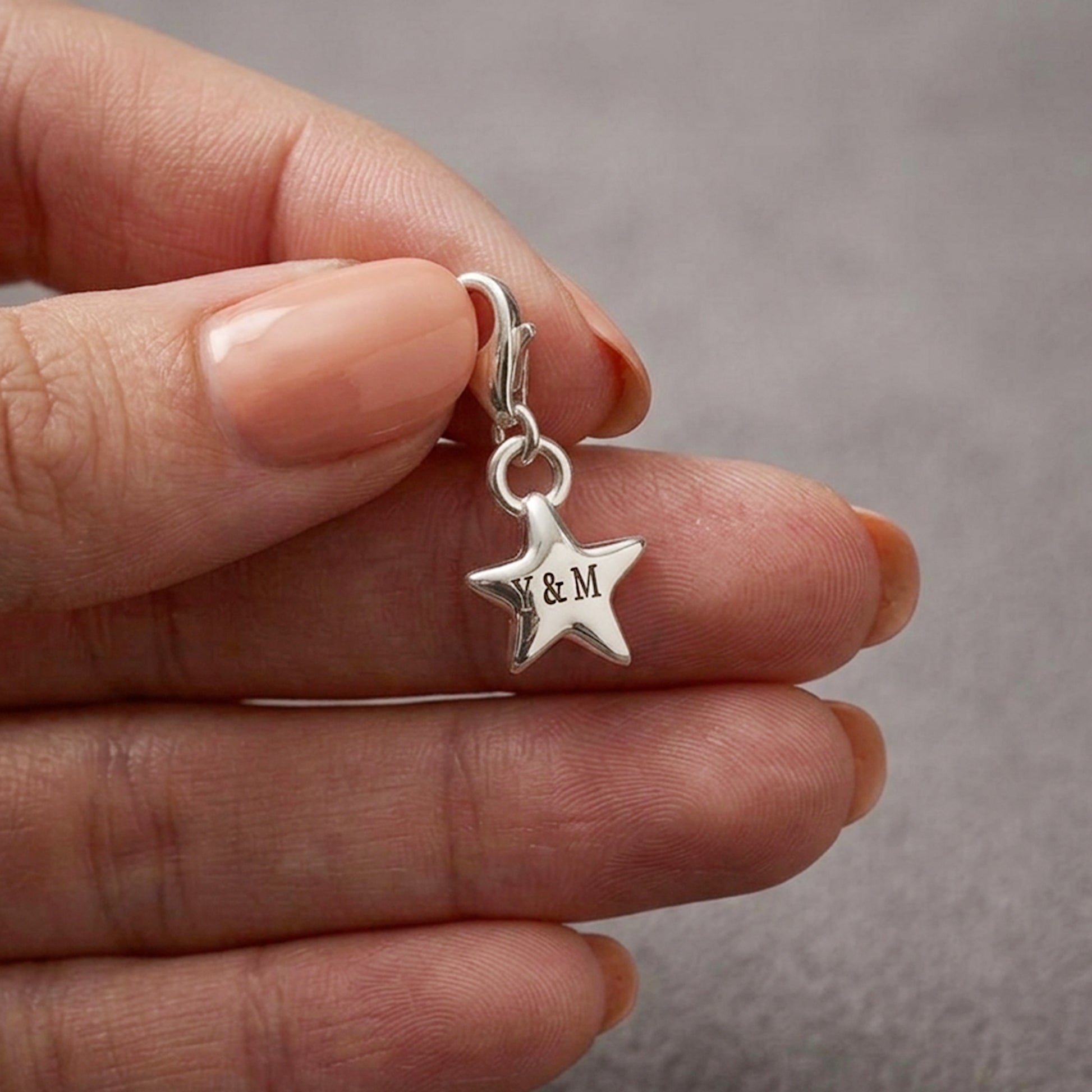 Silver star-shaped charm with initials held between fingers against a neutral background