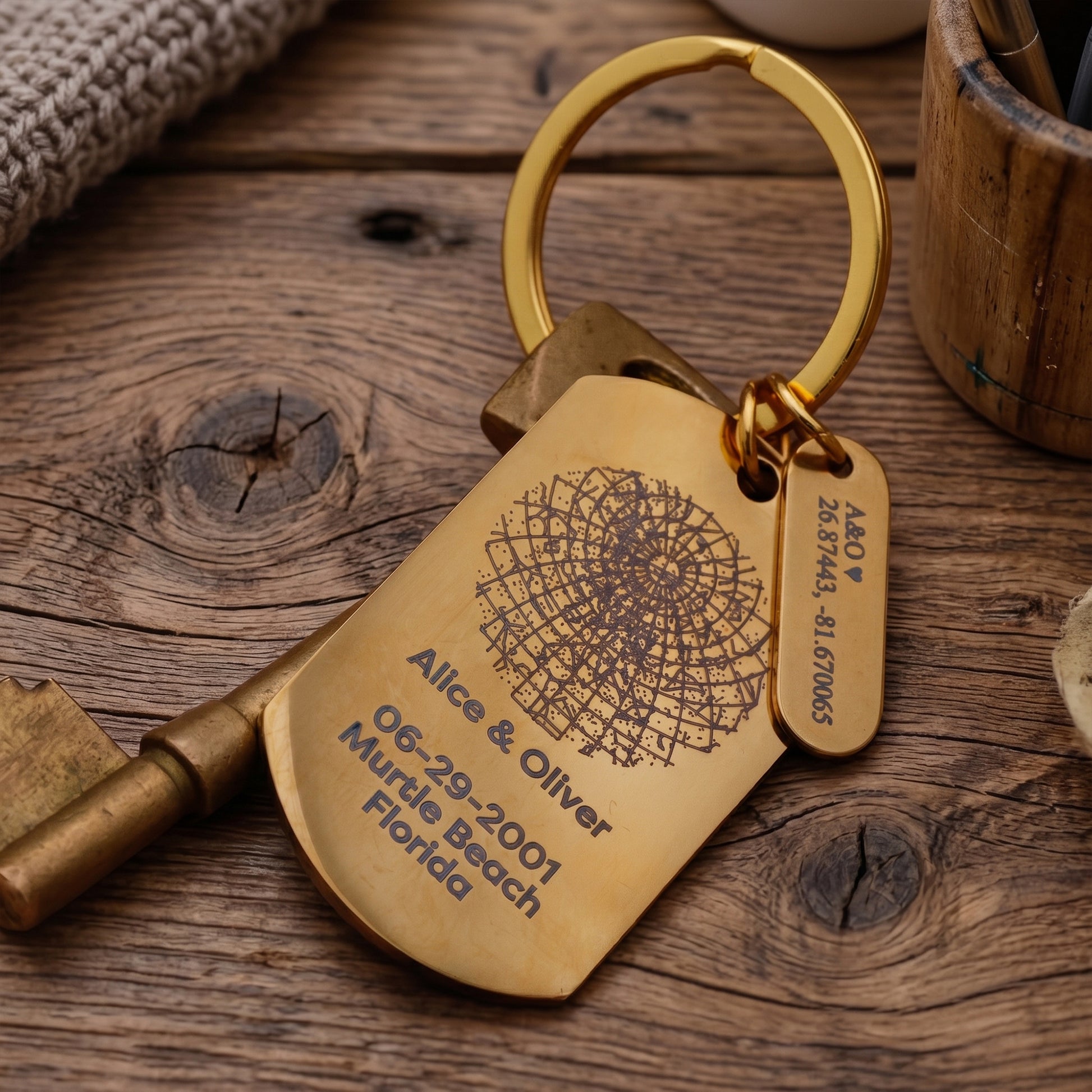 A personalized brass keychain with a dog tag and key, engraved with a Ferris wheel design and the name 'Alice & Oliver' with a date and location, resting on a rustic wooden surface.