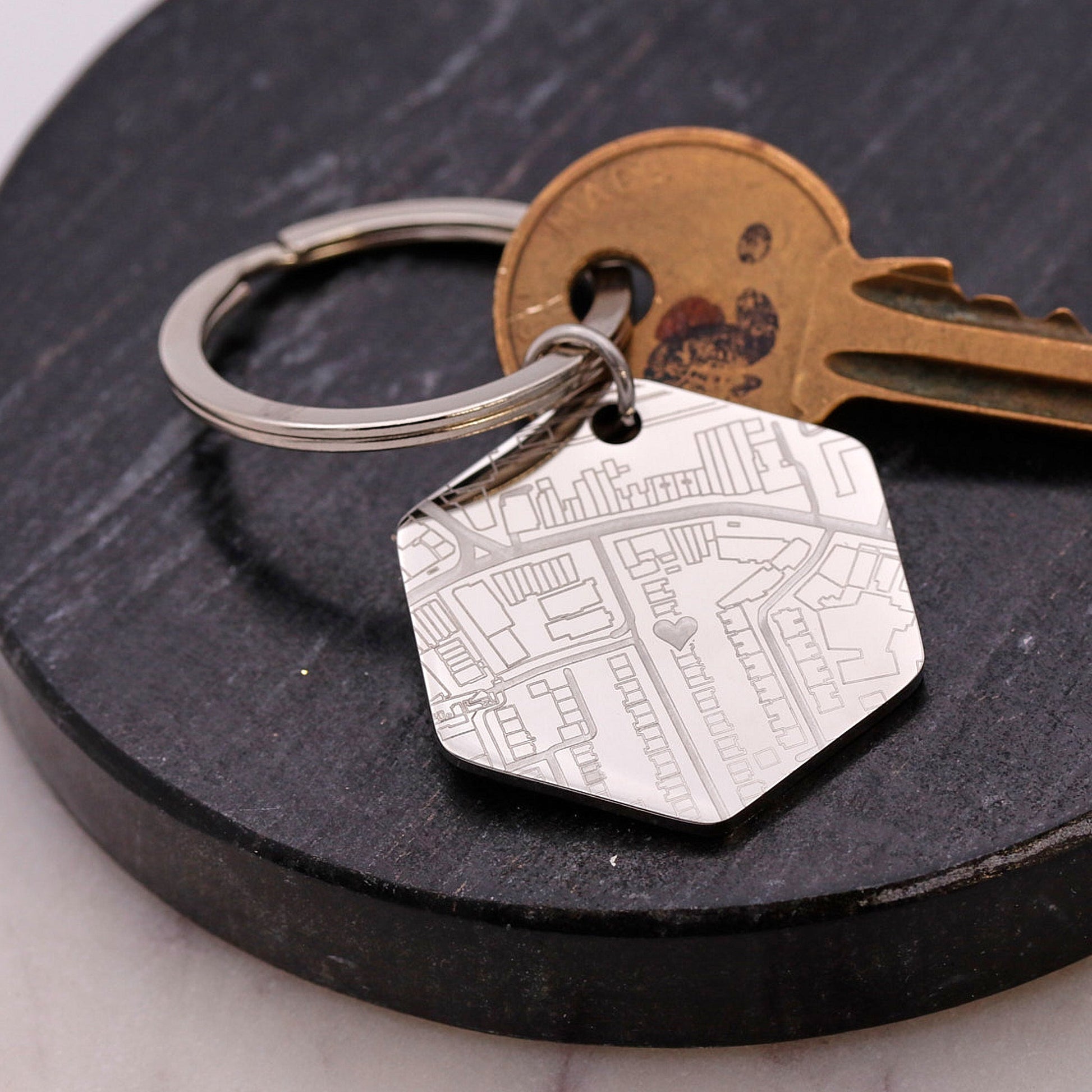 Hexagonal silver keychain with engraved map design on a dark surface with a key.