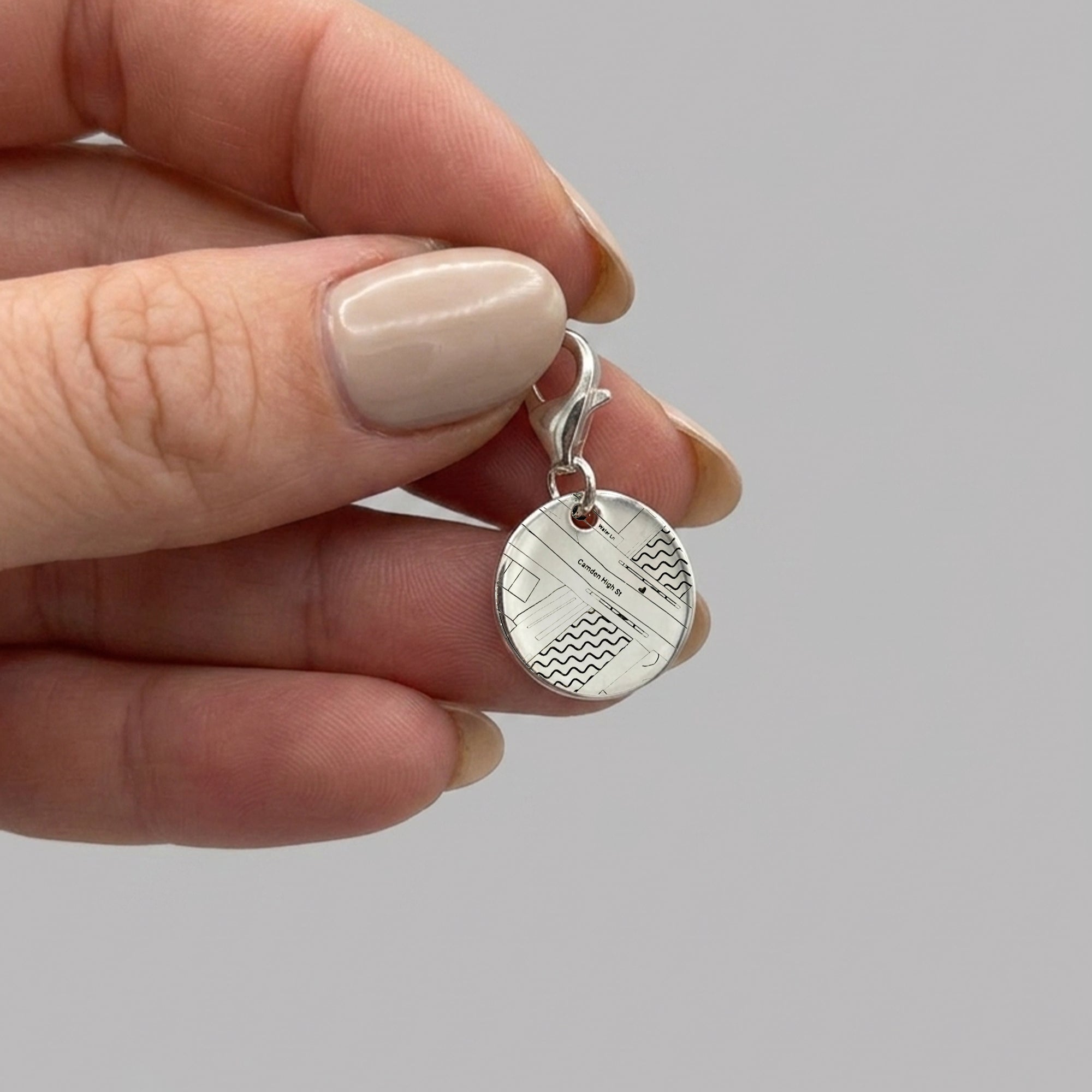 Silver pendant with geometric design held by a hand against a gray background