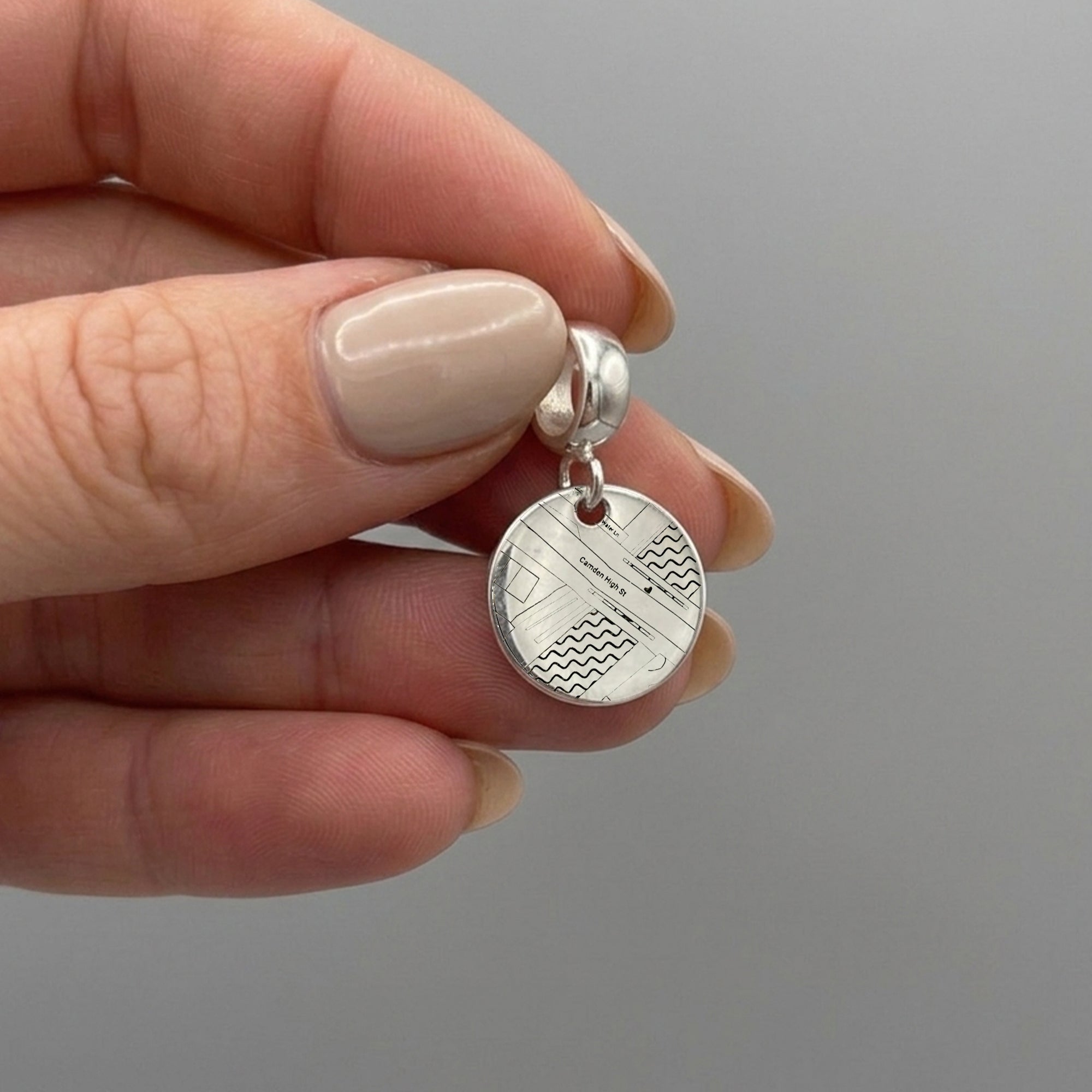 Silver earrings with circular designs held between fingers against a gray background