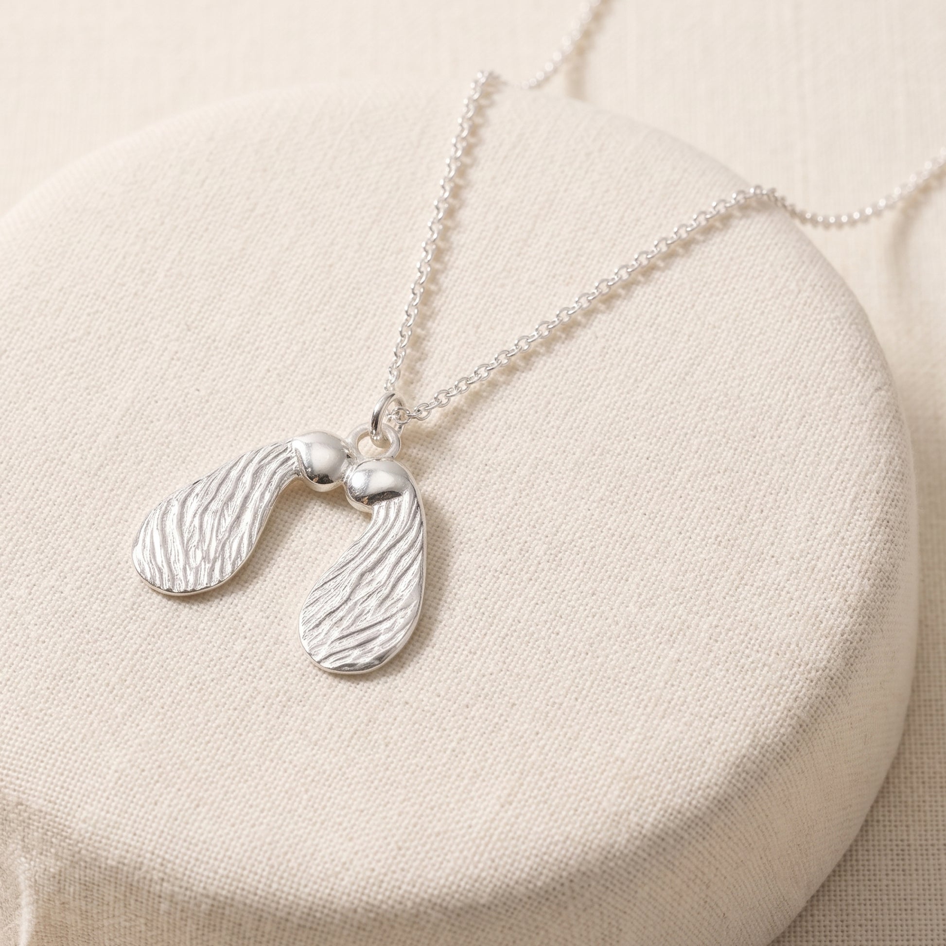 Silver necklace with a seed pod pendant on a beige surface