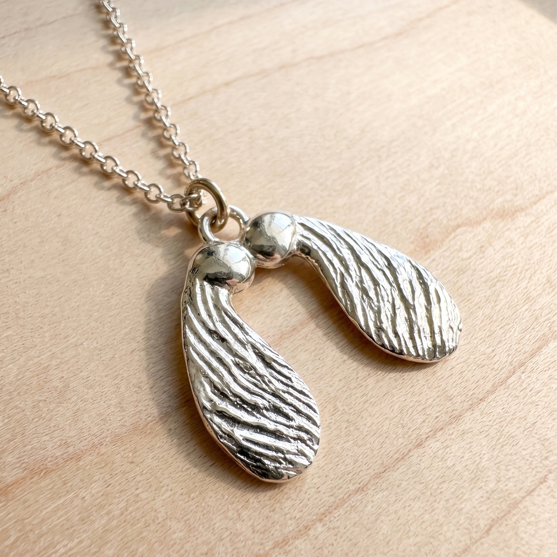 Silver pendant necklace with two leaf-shaped pendants on a wooden surface