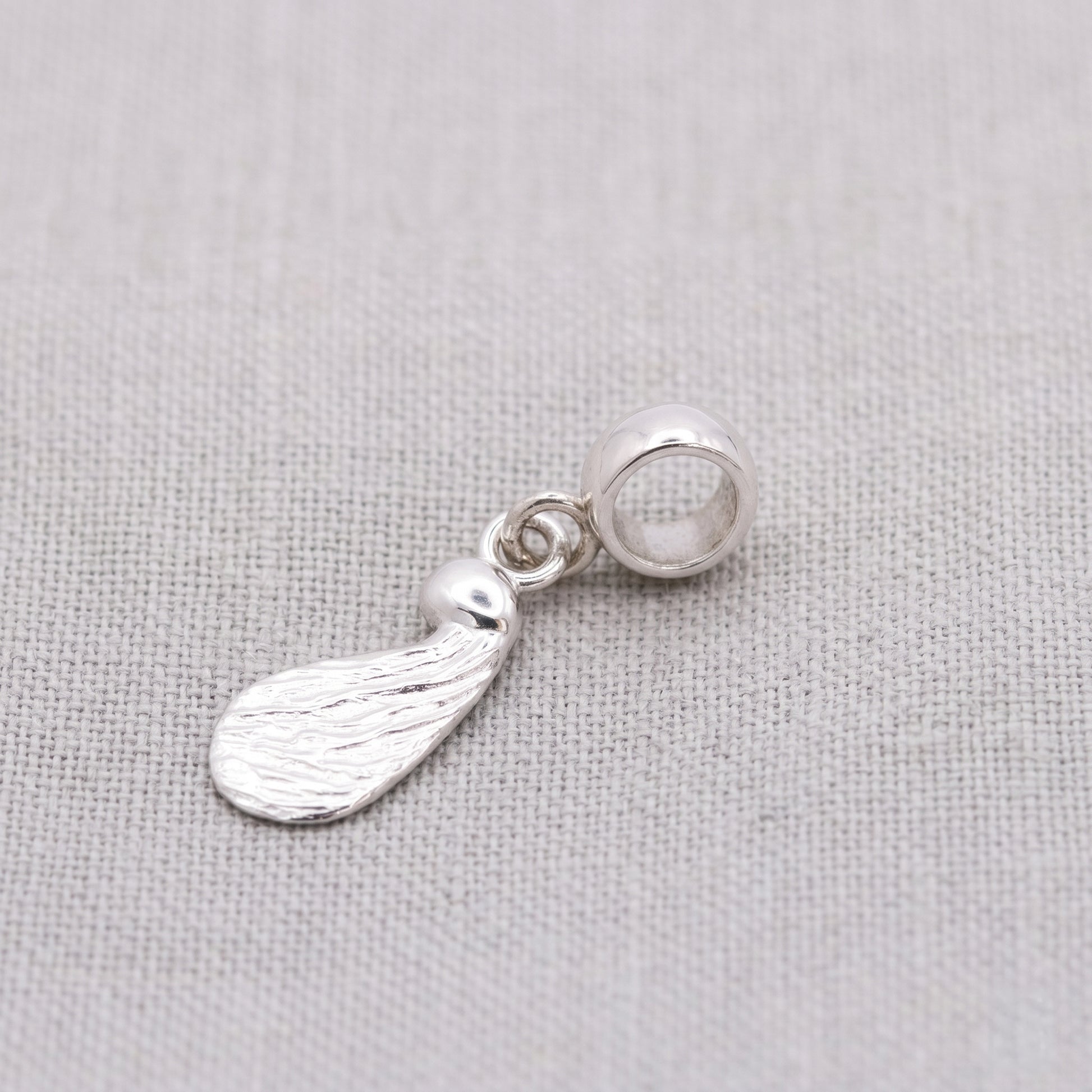 Silver pendant with a seed shape on a light gray fabric background