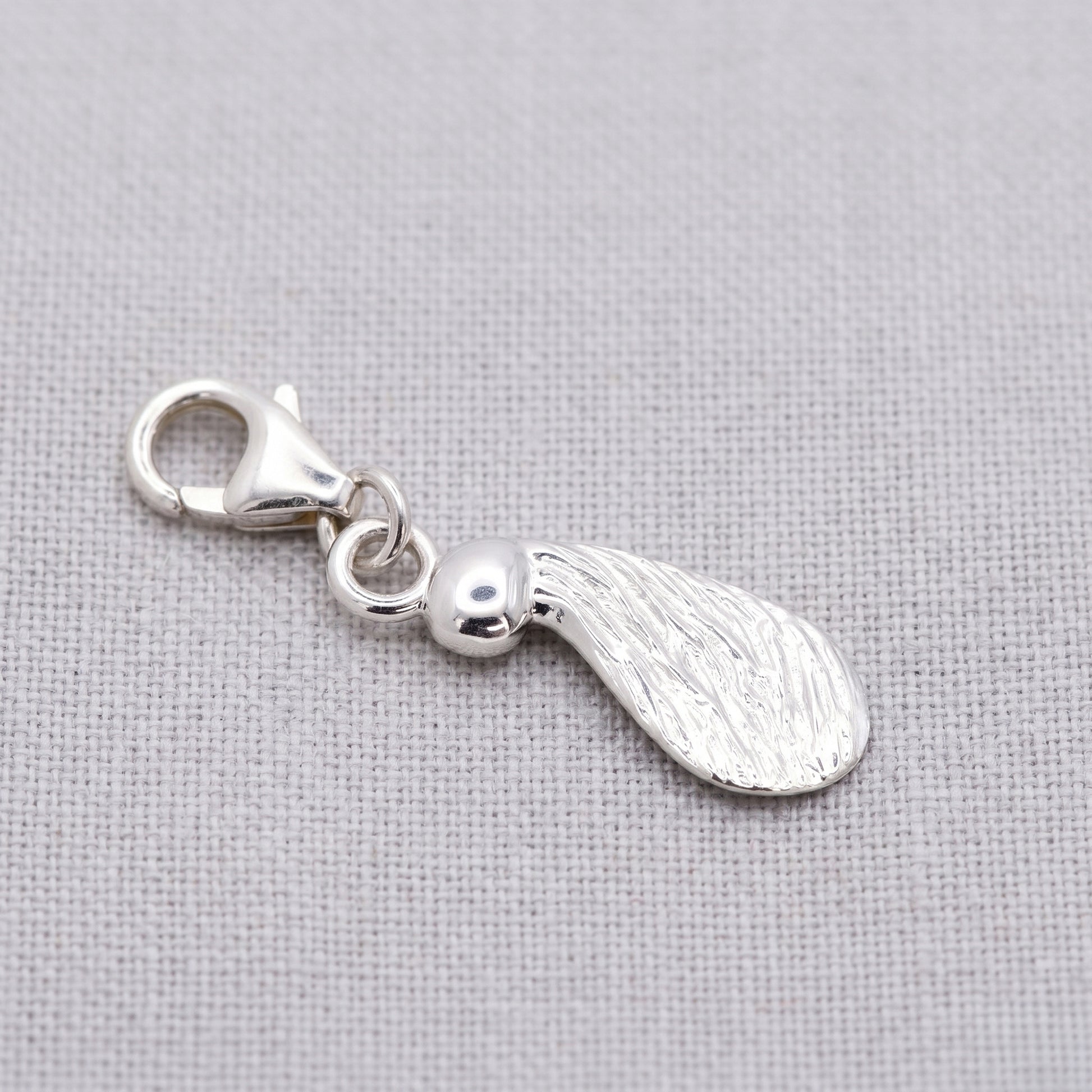 Silver seed-shaped pendant charm with a clip on a fabric background