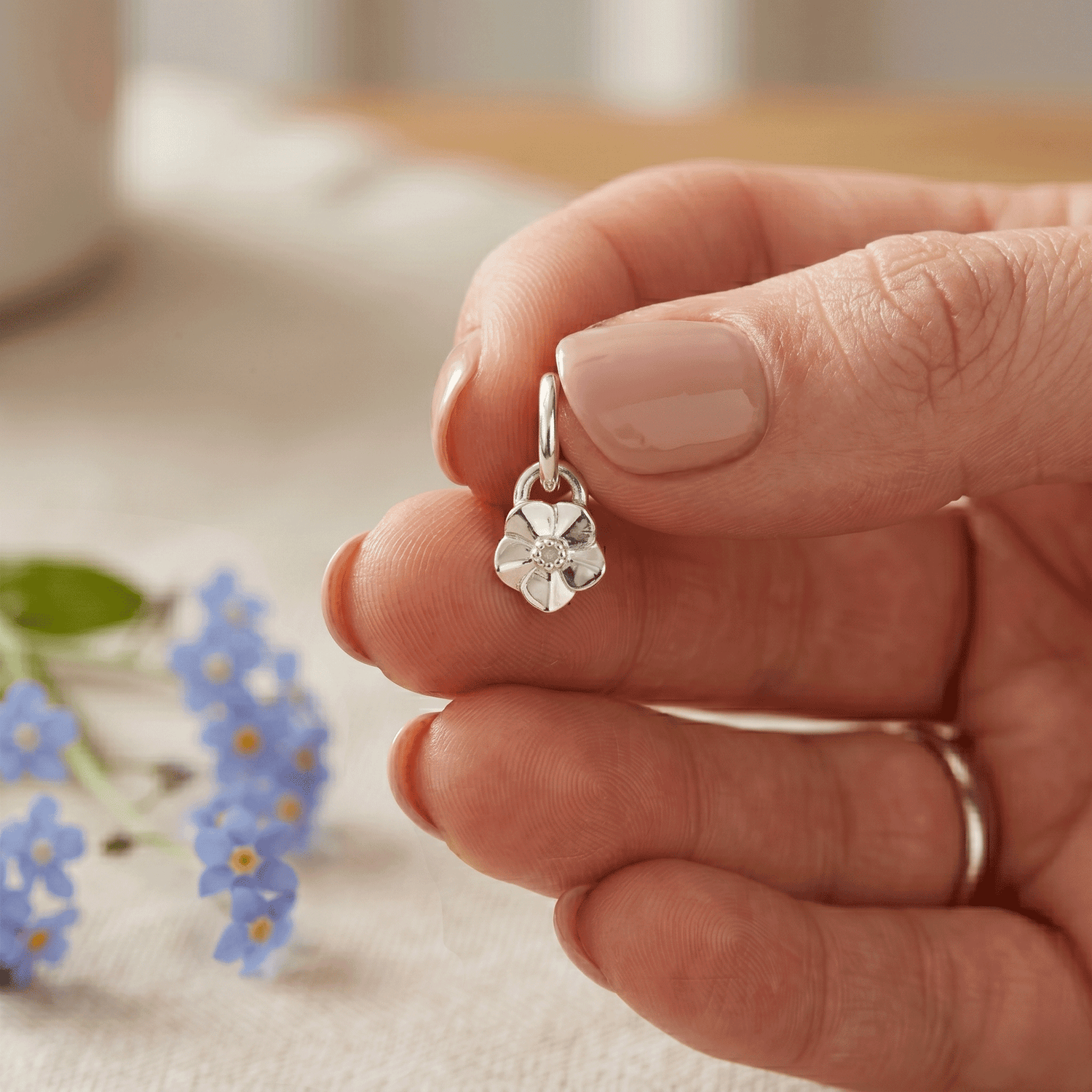 small sized silver flower charm in persons hands with flowers in the background
