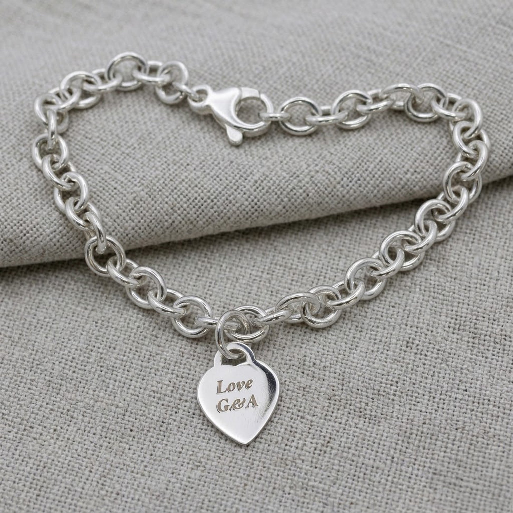 Silver bracelet with a heart-shaped tag on a gray fabric background