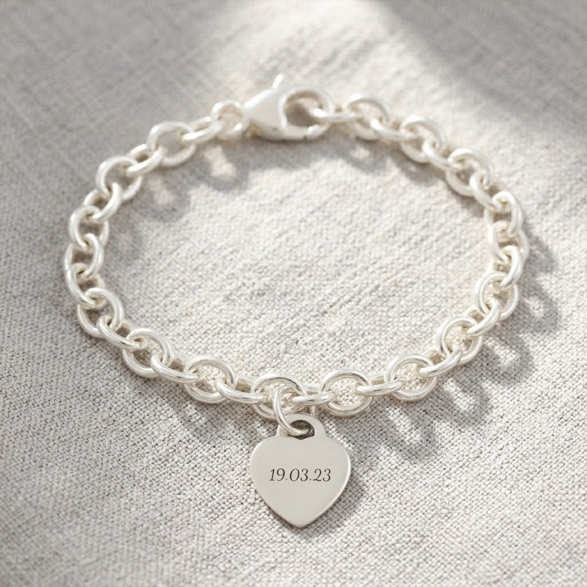 silver charm bracelet with engraved heart charm on a fabric background