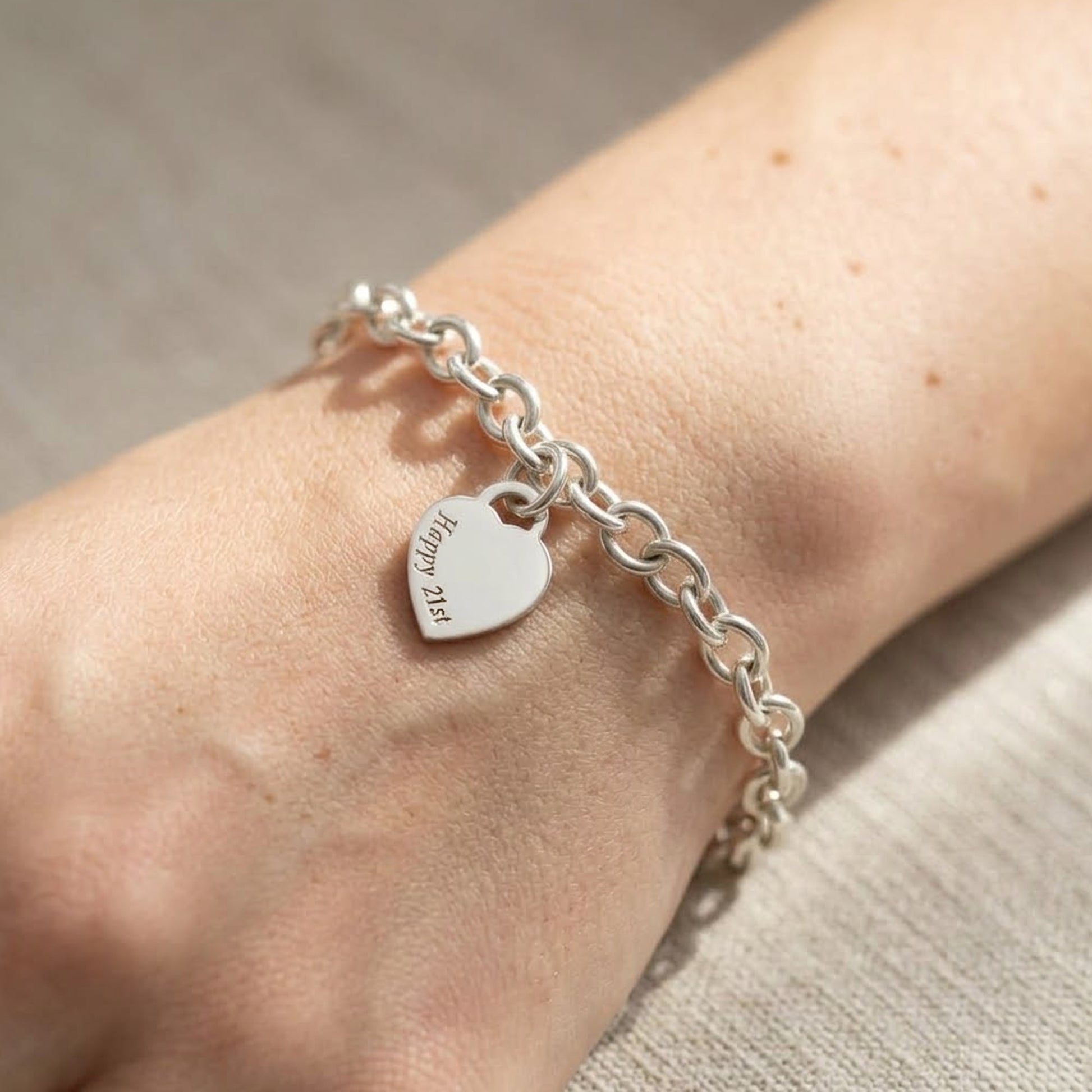 silver charm bracelet with engraved heart charm on a womans wrist