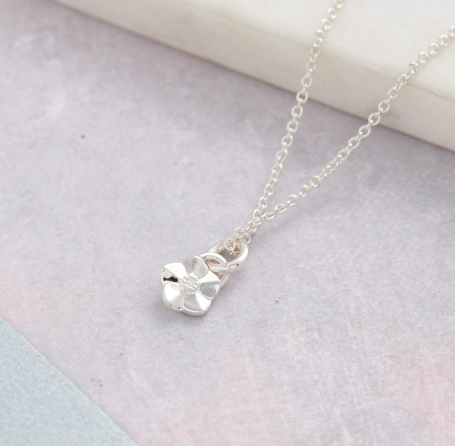 Silver necklace with a small flower pendant on a textured beige surface