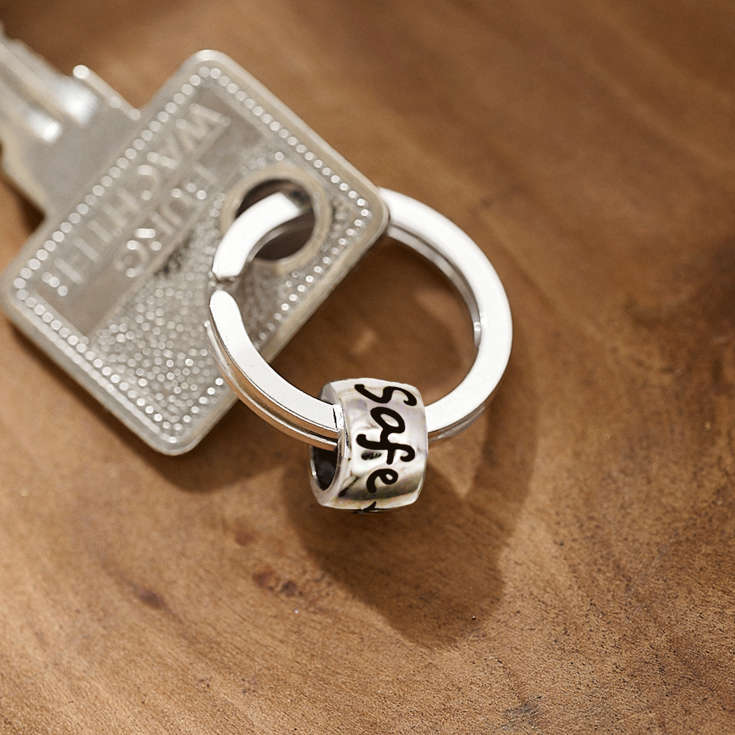 Silver keychain with a 'travel safe' charm on a wooden surface