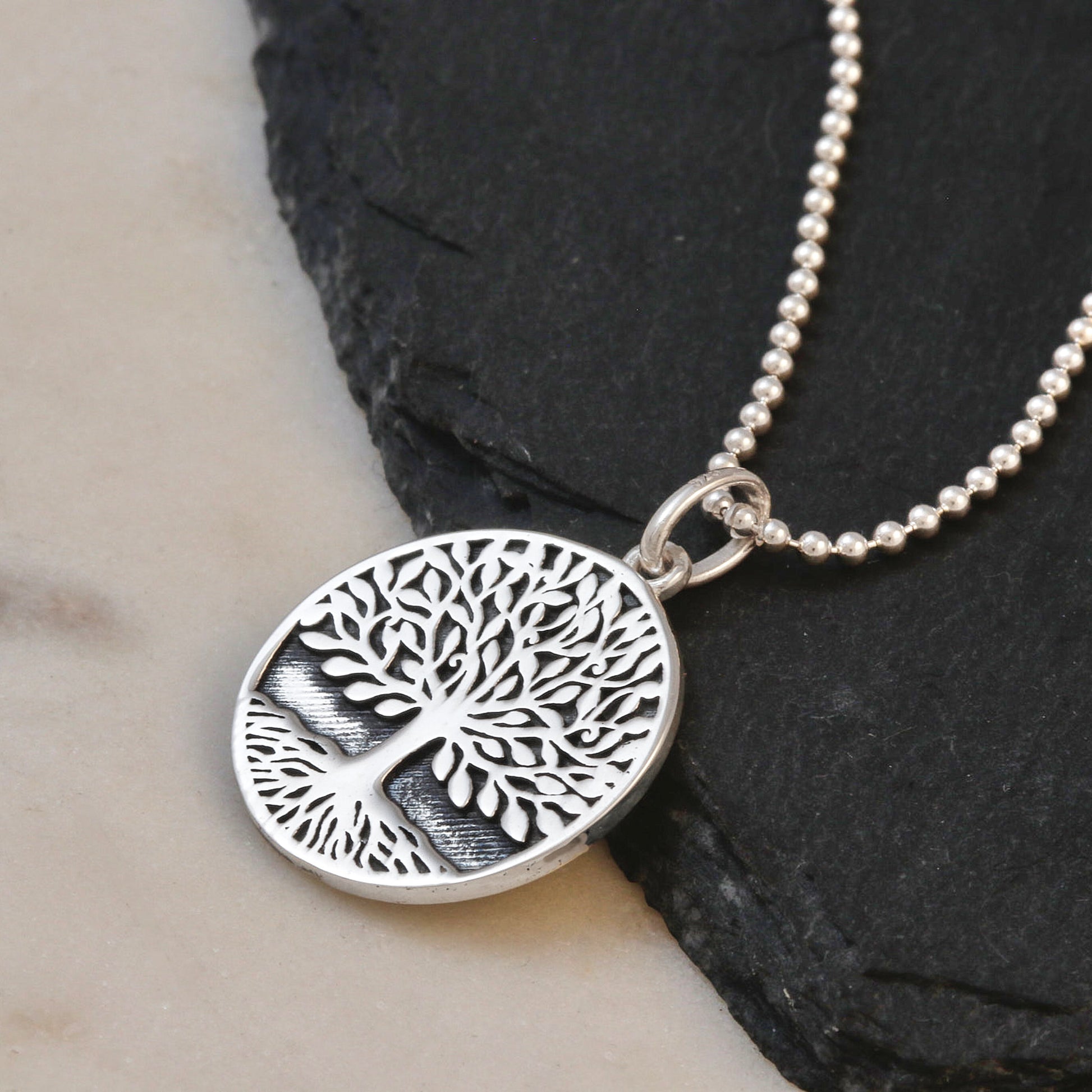 Silver tree of life pendant necklace on a dark stone surface