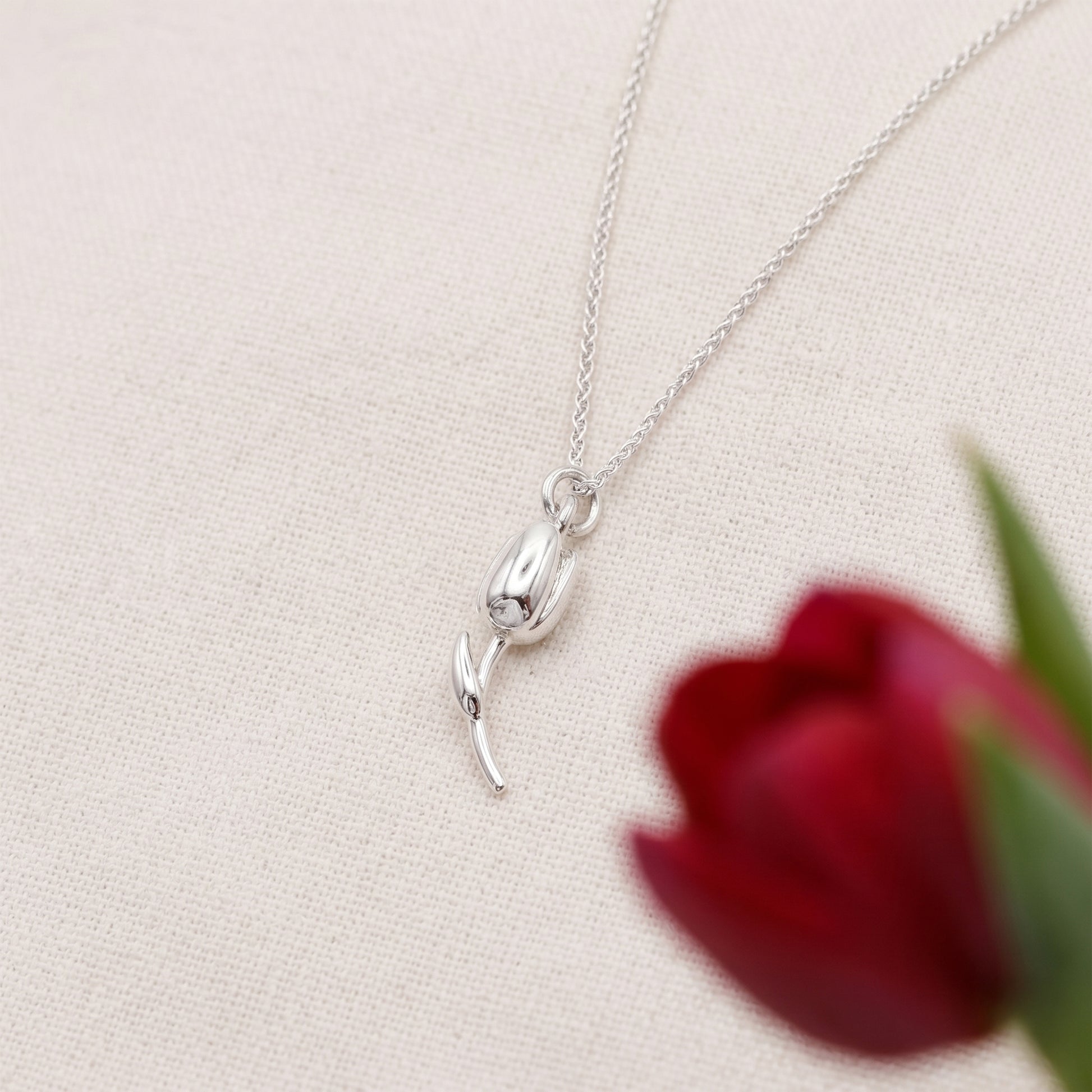 Silver necklace with a tulip pendant on a light beige background with a red tulip.