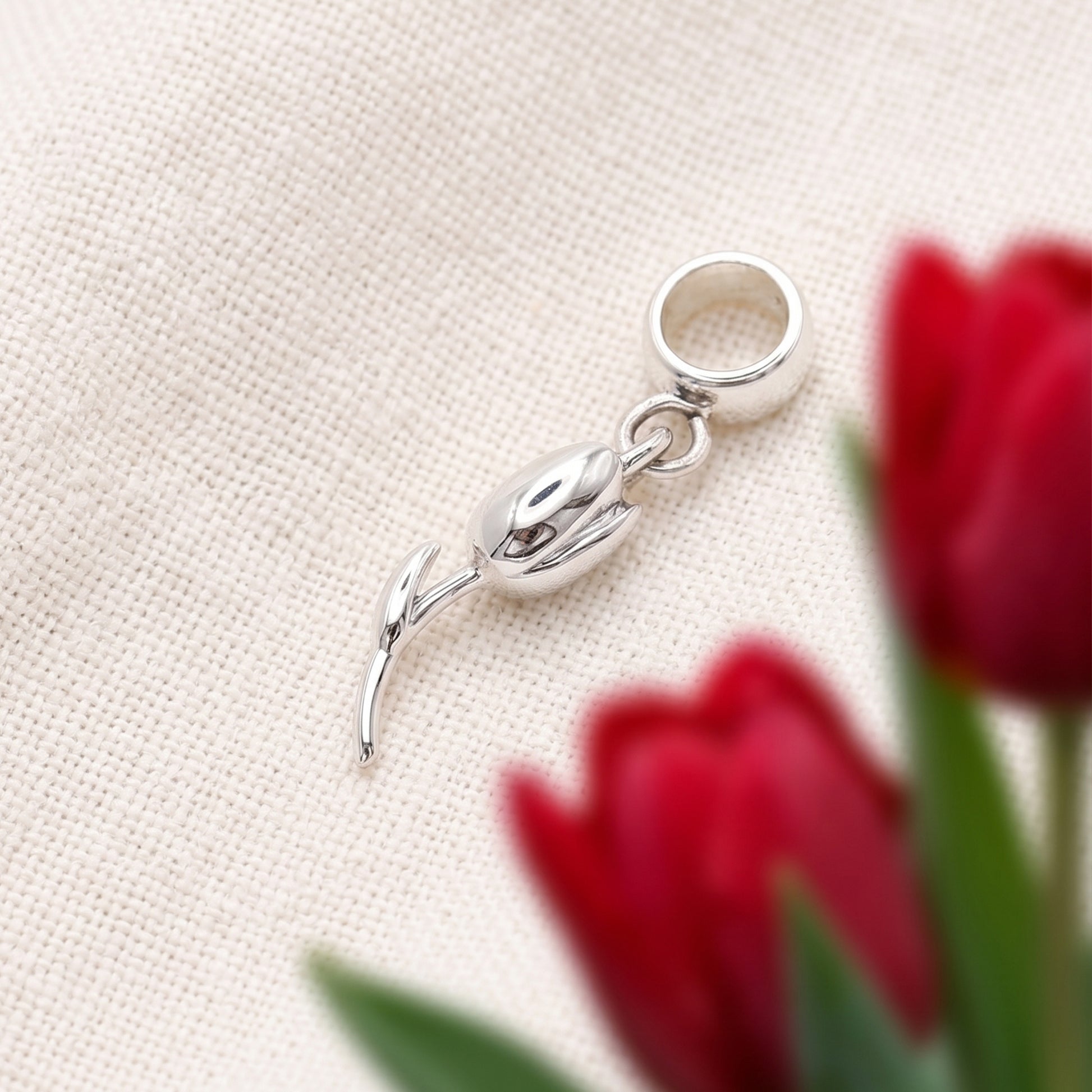 Silver pendant shaped like a tulip on a beige fabric background with red tulips.