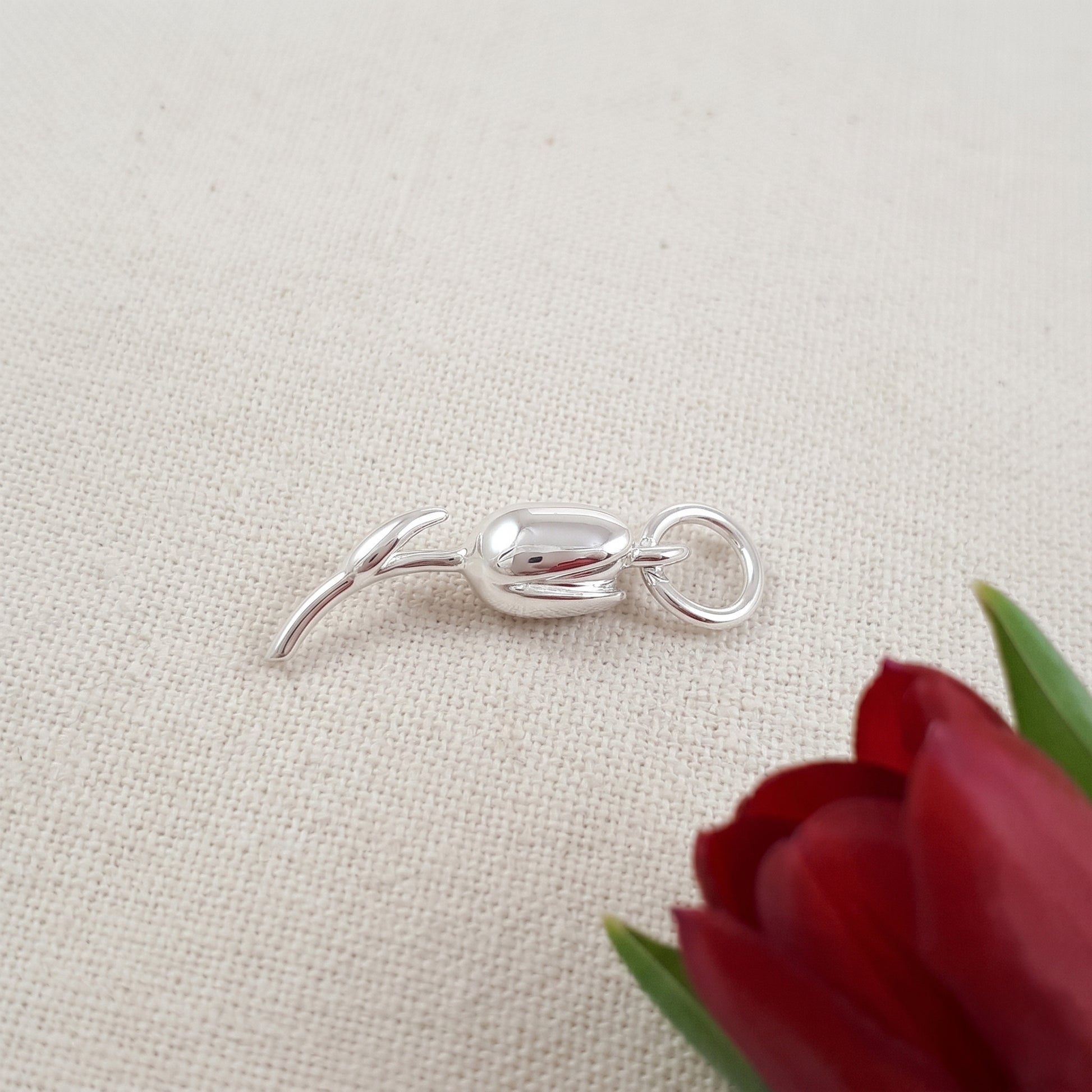 Silver tulip charm on a beige fabric background with a red tulip