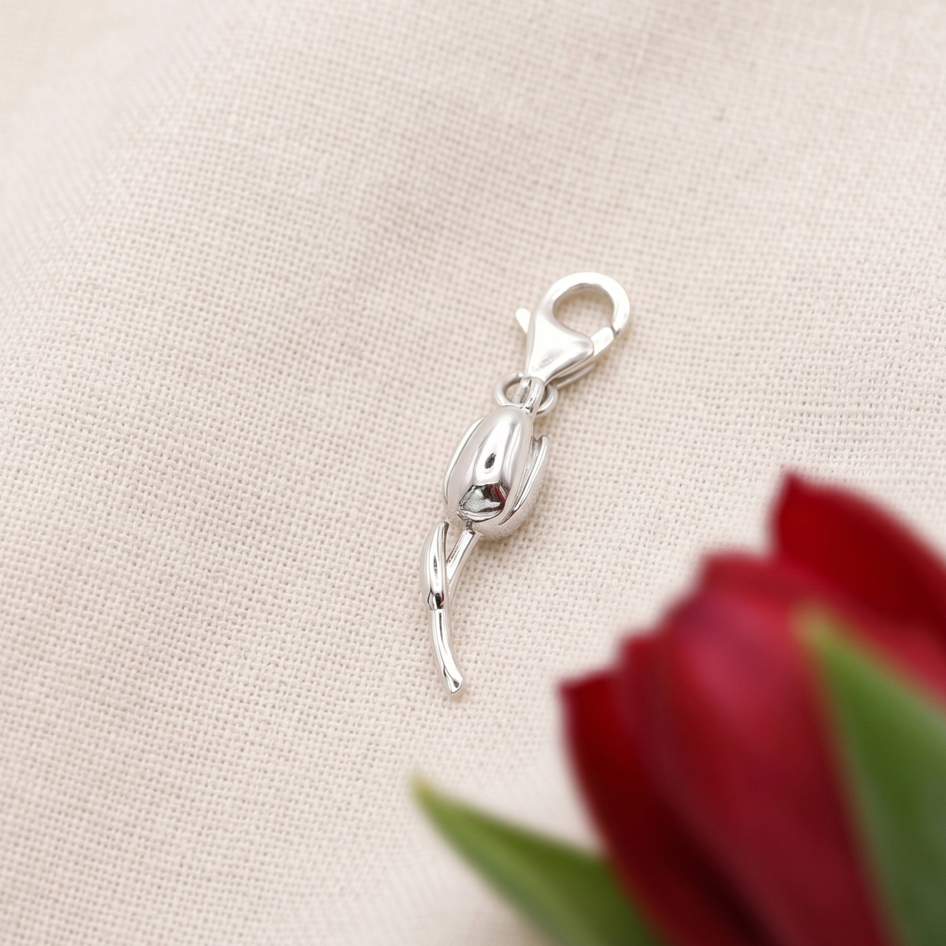 Silver clasp with tulip on a beige fabric background with a red flower.
