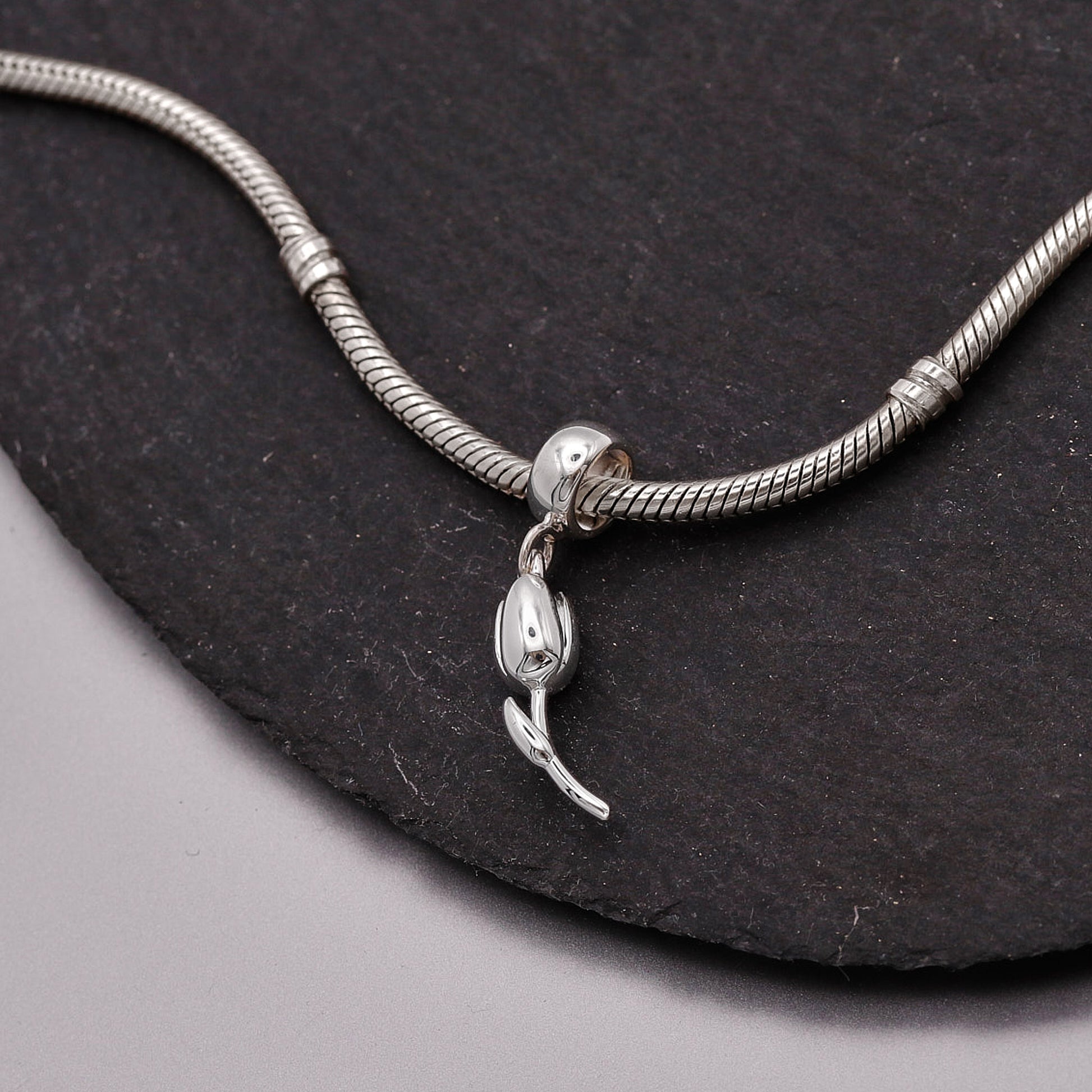 Silver snake chain bracelet with a lobster clasp on a dark stone surface