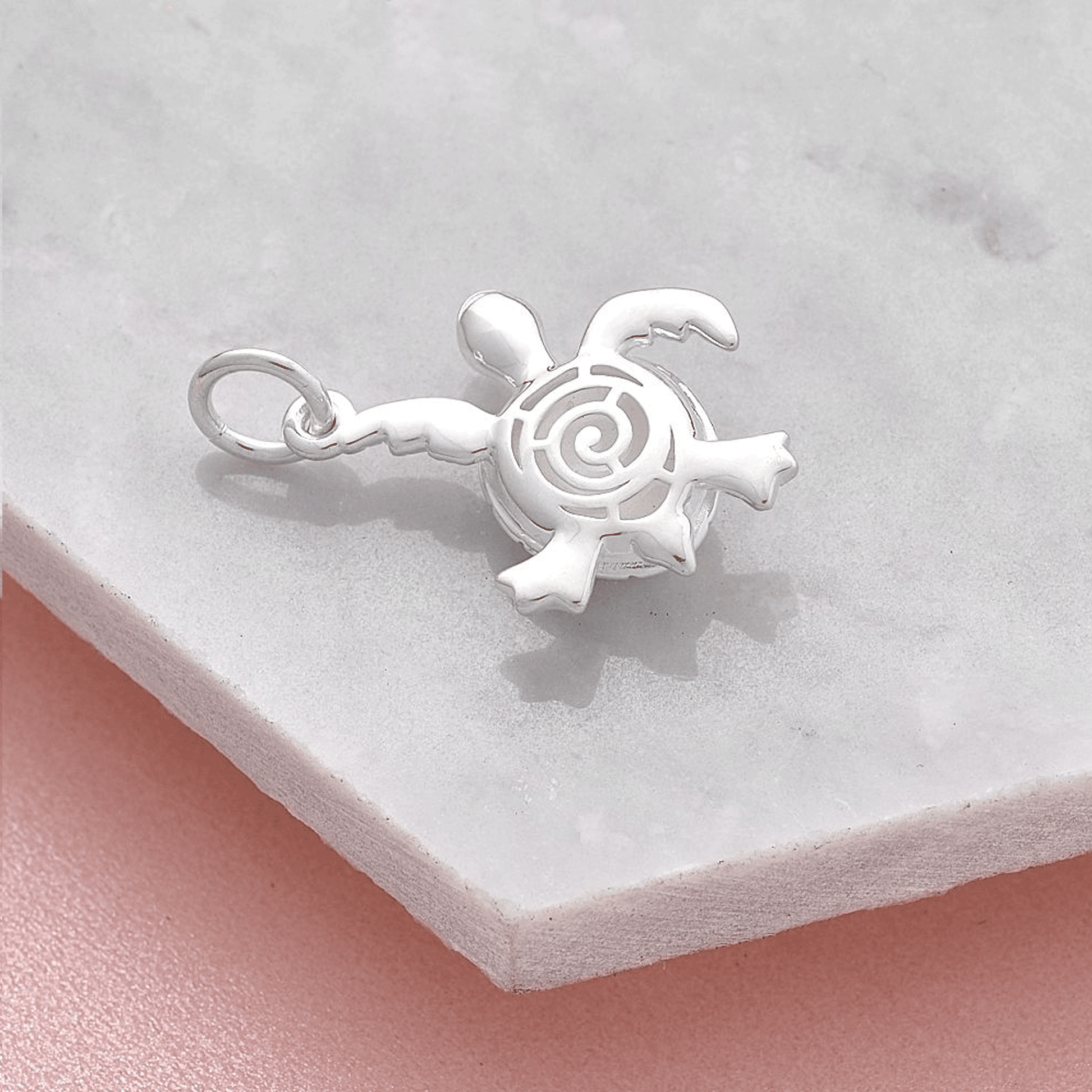 Silver turtle charm with shell reverse detail on a marble surface