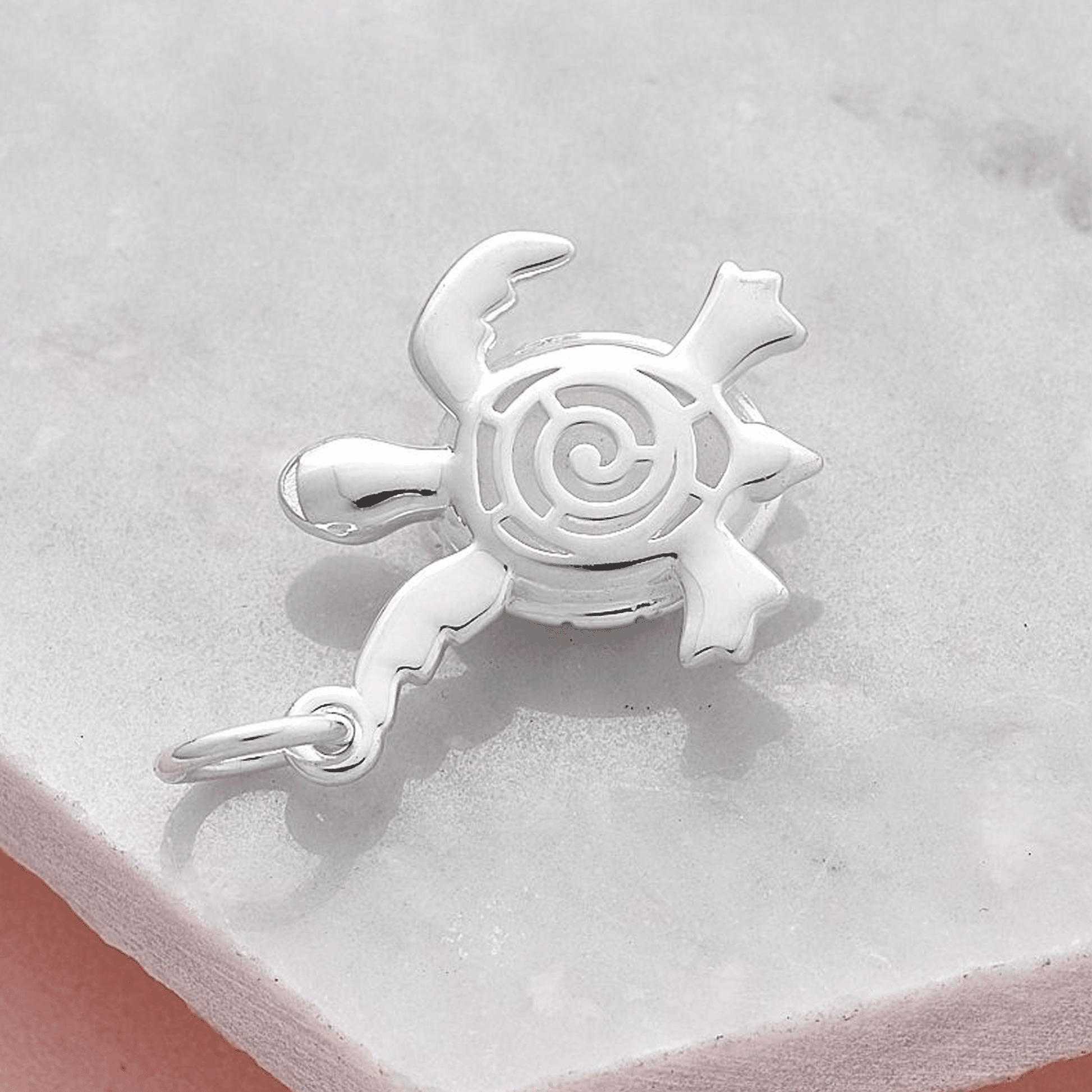 Silver turtle charm with shell reverse detail on a marble surface