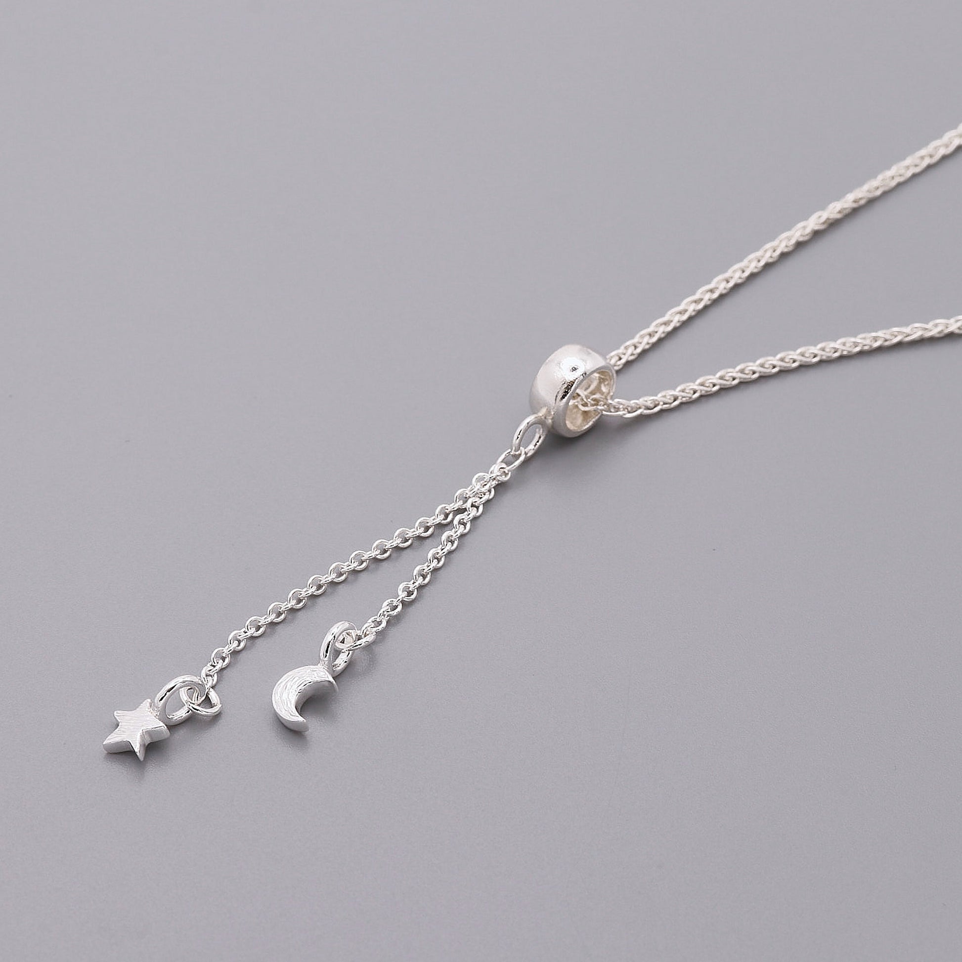 Silver necklace with star and moon charms on a gray background