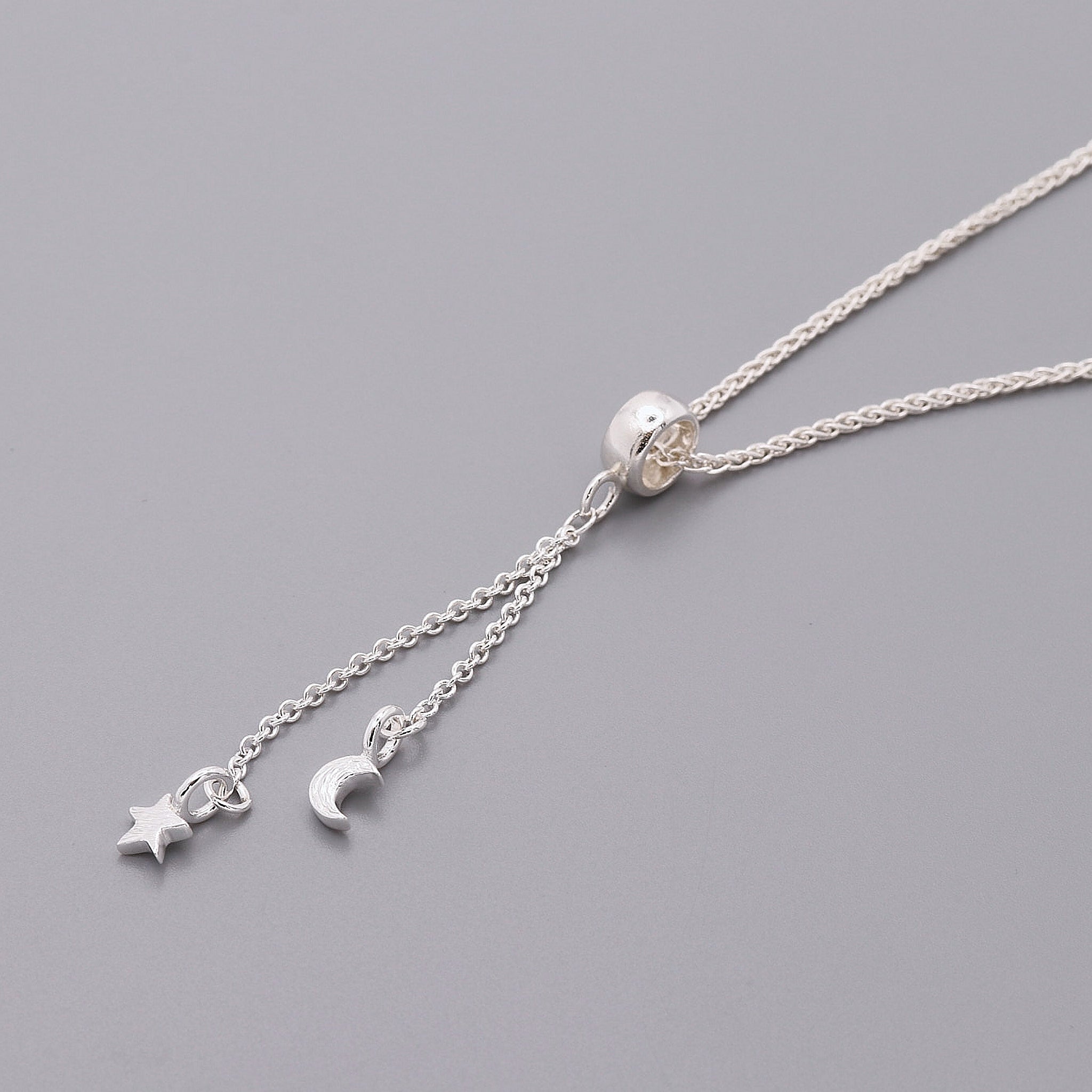 Silver necklace with star and moon charms on a gray background
