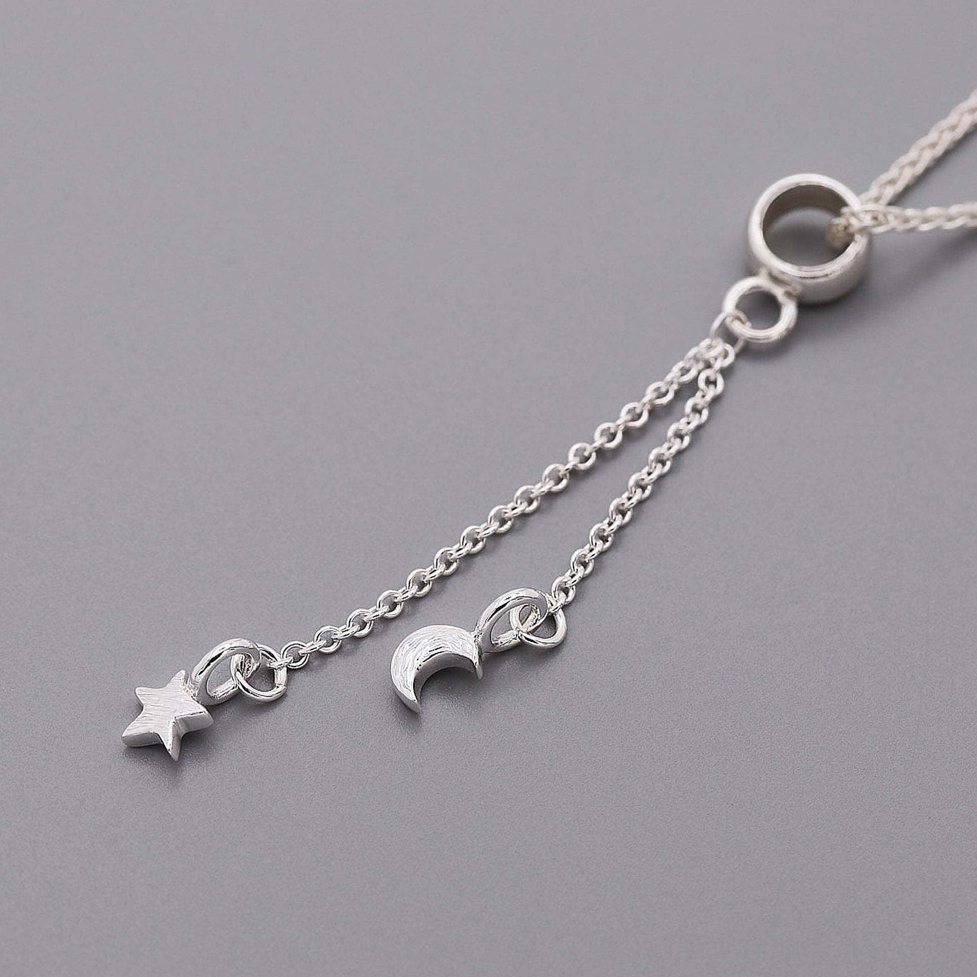 Silver necklace with star and moon charms on a gray background