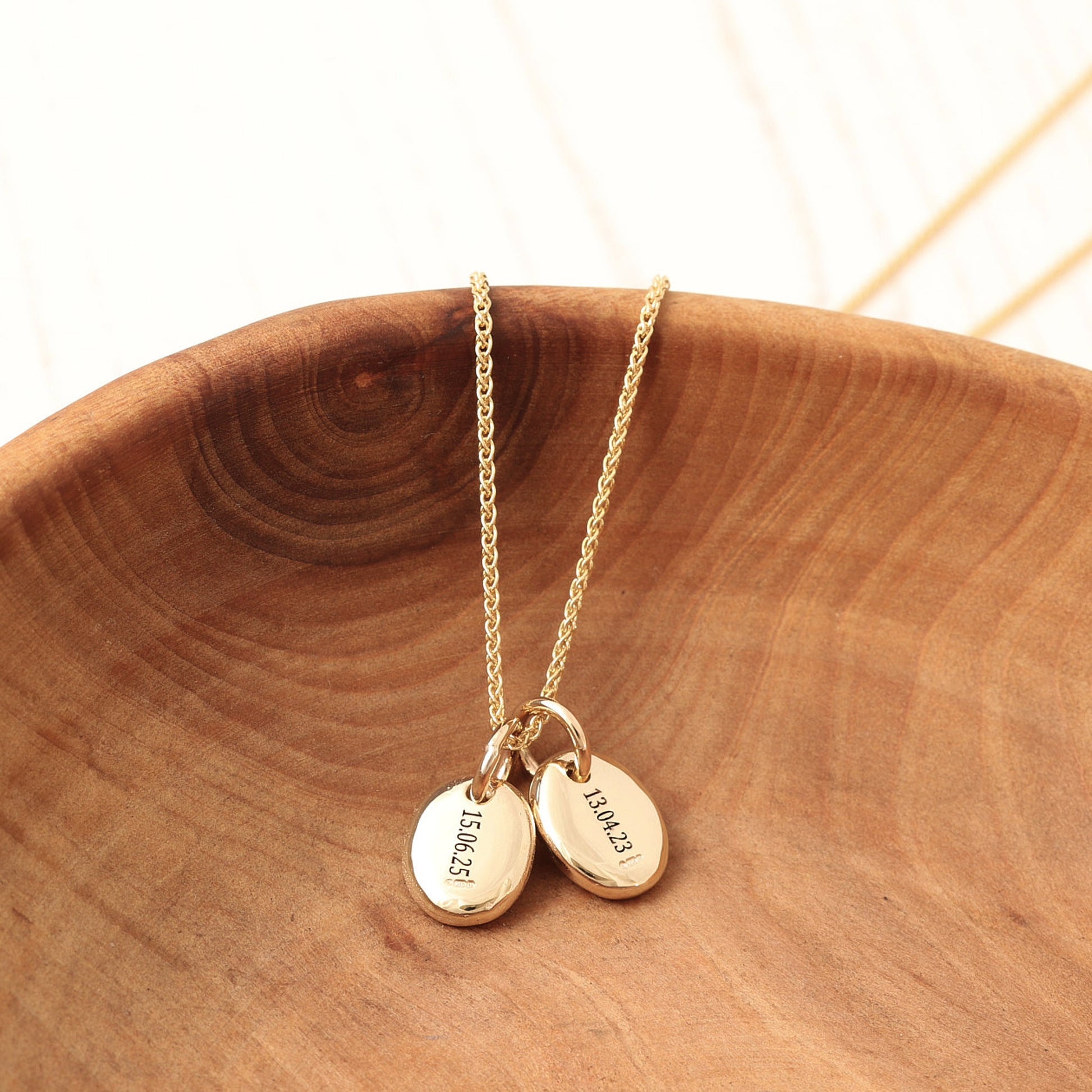 Gold necklace with two round pebble charms engraved on a wooden surface