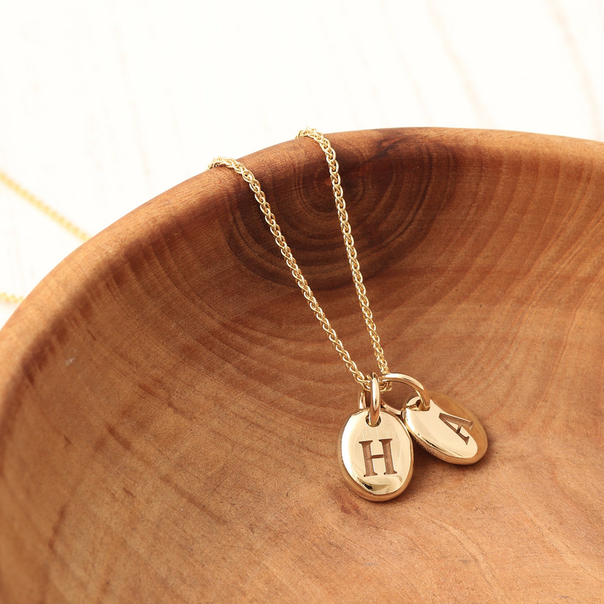 Gold necklace with two round pebble charms engraved on a wooden surface