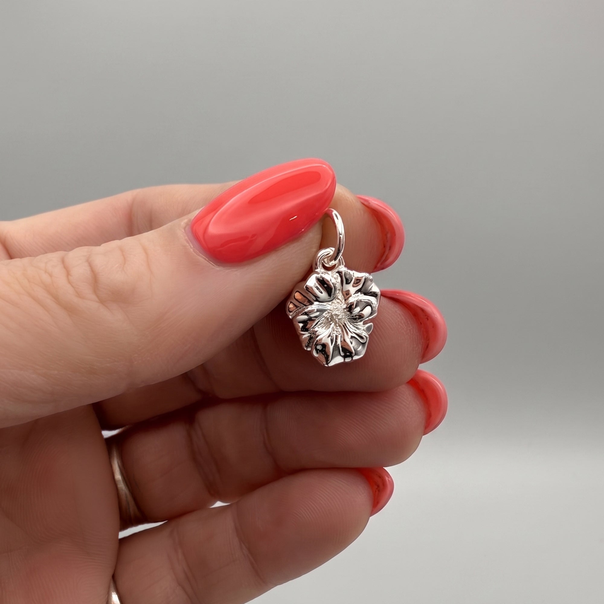 Silver floral pendant held by a hand with red nail polish on a gray background
