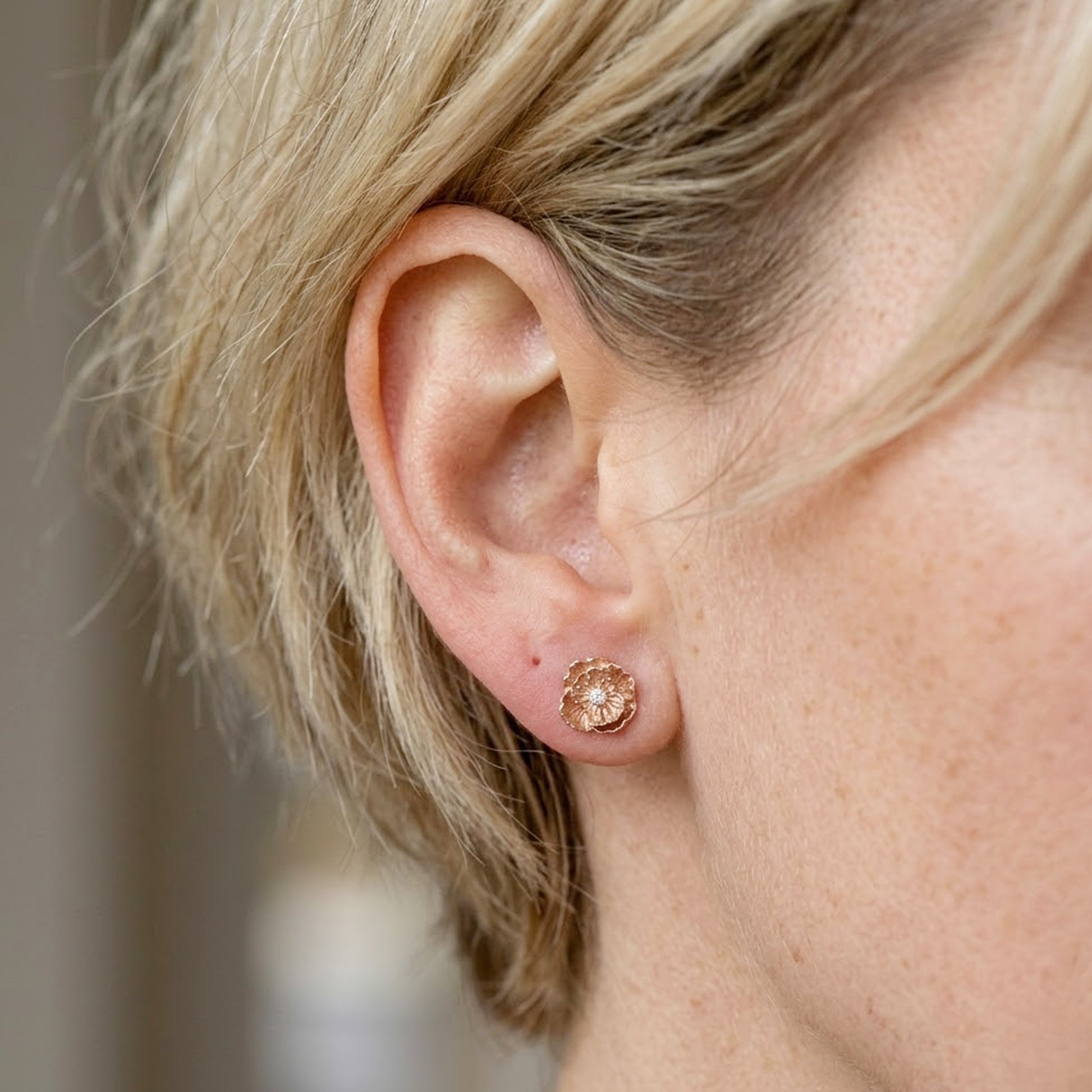 rose gold colour poppy studs in womans ear