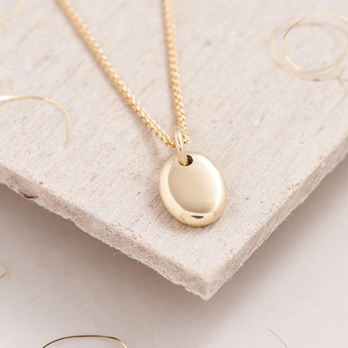 solid gold pebble charm as a pendant on a gold chain